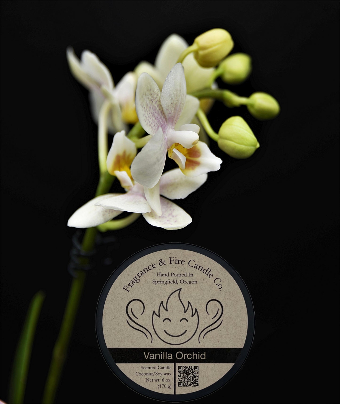 A Fragrance & Fire Candle Co. "Vanilla Orchid" scented candle sits below a cluster of delicate, pale yellow and white Phalaenopsis orchids with unopened green buds. The candle has a label featuring a smiling flame and the text "Vanilla Orchid," "Scented Candle," and "Coconut / Soy wax." The background is black.